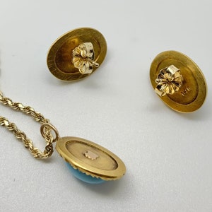 May include: A gold necklace with a turquoise pendant and matching earrings. The pendant and earrings are oval shaped with a gold border and a turquoise stone in the center. The back of the earrings are marked with '14K'.