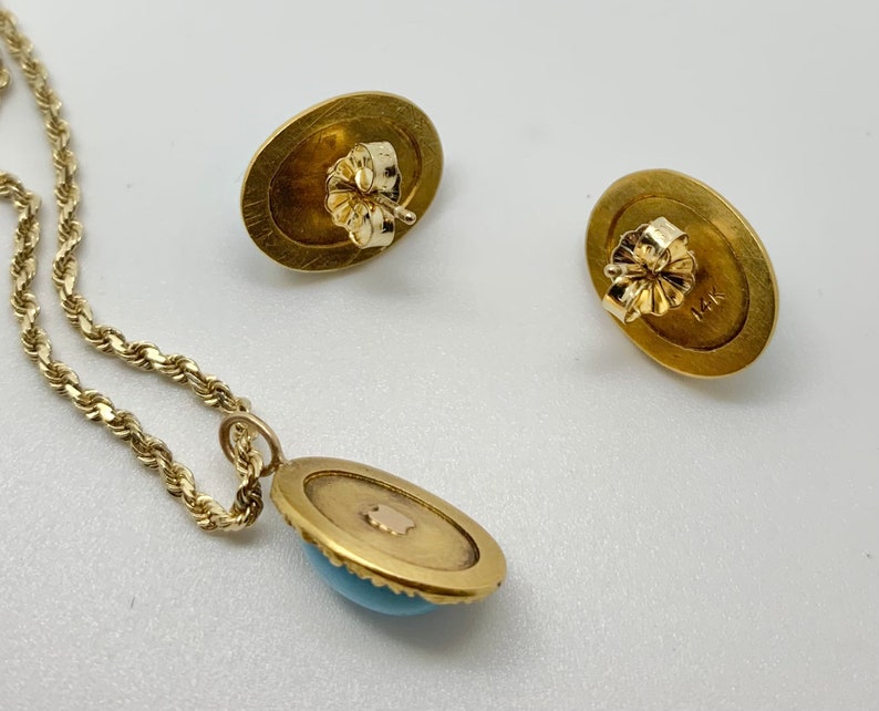 May include: A gold necklace with a turquoise pendant and matching earrings. The pendant and earrings are oval shaped with a gold border and a turquoise stone in the center. The back of the earrings are marked with '14K'.