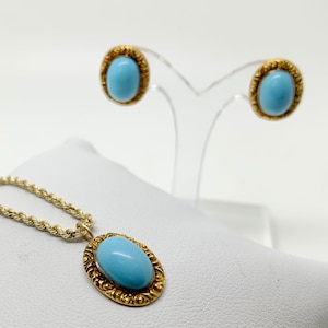 May include: A gold necklace with a light blue oval stone pendant and matching earrings. The pendant and earrings have a detailed gold filigree design.