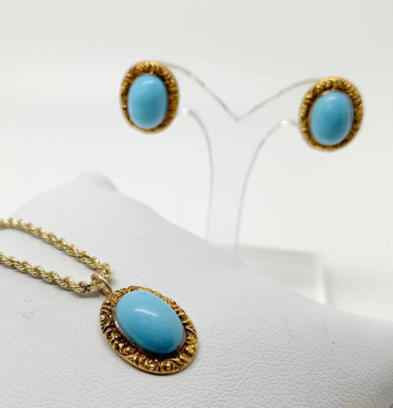 May include: A gold necklace with a light blue oval stone pendant and matching earrings. The pendant and earrings have a detailed gold filigree design.