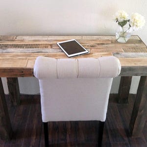 May include: A rustic wooden desk with a white upholstered chair. The desk is made from reclaimed wood planks and has a natural wood finish. A tablet computer is sitting on the desk.
