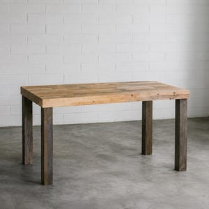 May include: A rectangular dining table featuring a thick, light brown natural wood grain tabletop surface supported by four sturdy, dark brown square wooden legs. The table has a clean, simple construction with visible wood texture throughout.