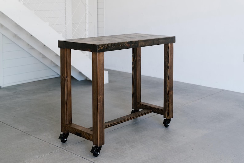Reclaimed wood bar table with U-shaped legs and locking caster wheels.