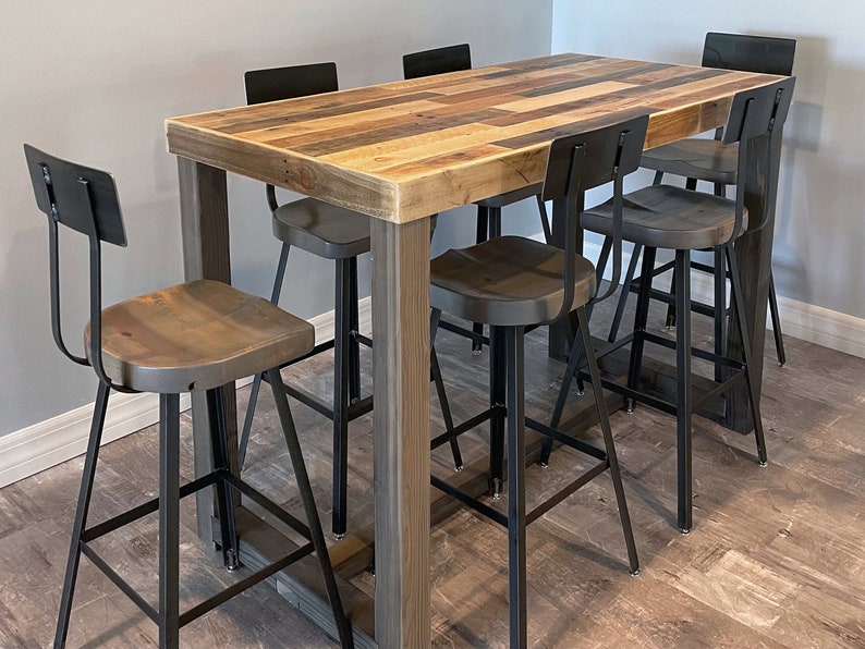 May include: A rustic bar table with a reclaimed wood top and gray wooden legs. It is surrounded by five metal bar stools with wooden seats and black metal frames. The table and stools are set on a wood-look floor.