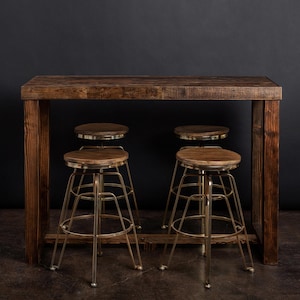 May include: A rustic wooden bar table with a dark brown finish and four gold metal bar stools. The table has a rectangular top and a simple, industrial design.