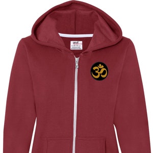 May include: A maroon zip-up hoodie with a black circle patch featuring a gold Om symbol.