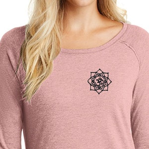 May include: A long-sleeved, pink shirt with a black Om symbol design on the front. The shirt has a relaxed fit and a rounded hem.
