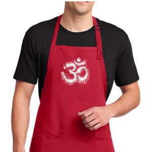 Puede incluir: Delantal rojo con un diseño de símbolo Om en tie-dye blanco. El delantal tiene un bolsillo grande en la parte delantera.