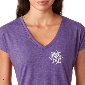 May include: A purple V-neck t-shirt featuring a white Om symbol. The top has short sleeves and a relaxed fit. The fabric has a heathered texture. The shirt is a casual style.