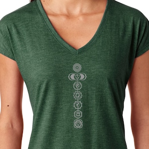 May include: A green v-neck t-shirt with a white graphic of the seven chakras. The chakras are aligned vertically in a column, with the root chakra at the bottom and the crown chakra at the top.