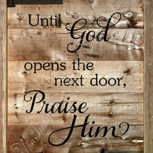 May include: Wooden sign with the message "Until God opens the next door, Praise Him in the hallway." The sign has a rustic, farmhouse style with black text and hinges.