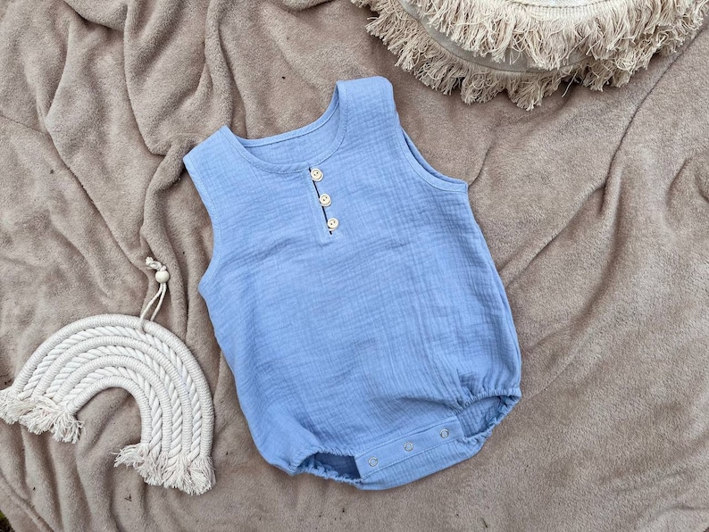 May include: A light blue sleeveless baby onesie with a button closure and snap closures at the bottom. The onesie is made of a soft, textured fabric.