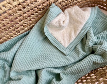 May include: A soft, light green waffle weave throw blanket with a white fleece lining. The blanket is folded and displayed in a woven basket.