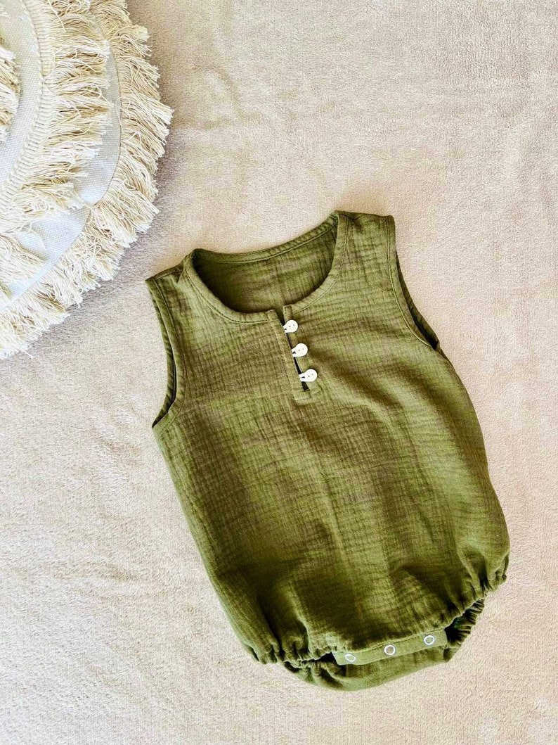 May include: A green sleeveless baby onesie with white button closures. The onesie has a gathered bottom.
