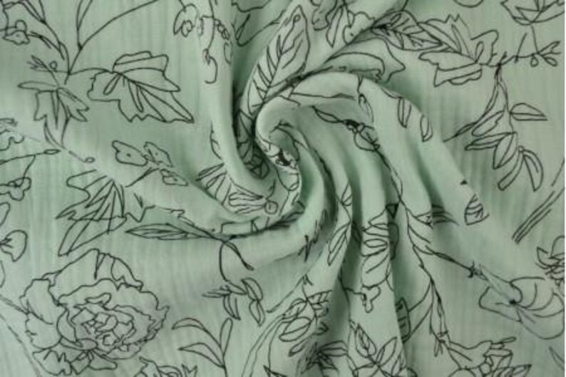 May include: A close-up of a light green fabric with a floral pattern. The fabric has a crinkled texture and is adorned with black outlines of flowers, leaves, and stems. The design is evenly distributed across the material, creating a delicate and artistic look.
