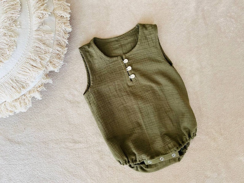 May include: A sleeveless, olive green baby onesie with white button closures. The onesie is made of a soft, textured fabric.