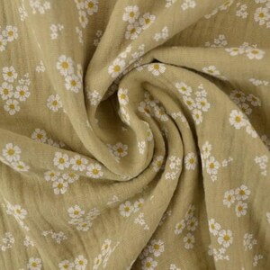 May include: Close-up of a folded fabric with a repeating floral pattern. The fabric is a muted olive green color, with small white flowers and yellow centers scattered across the surface. The fabric has a soft, textured appearance.