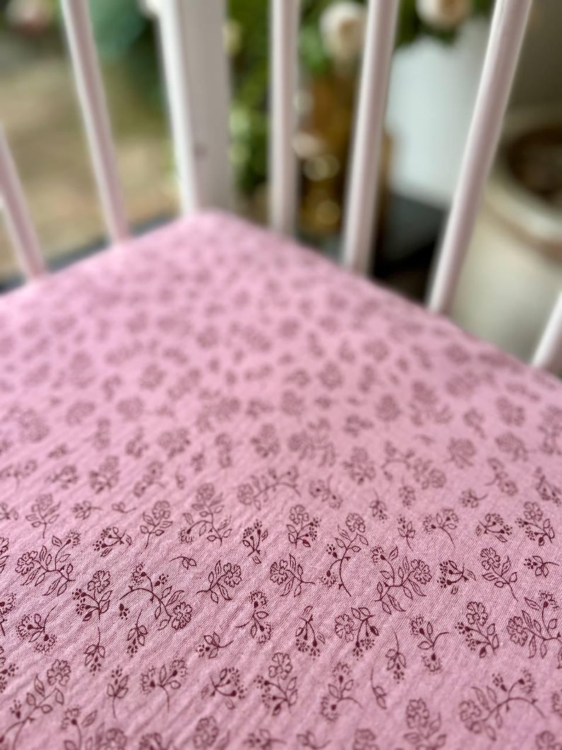 May include: Close-up of a pink fabric with a floral pattern. The fabric is a light pink color with a repeating pattern of small, dark brown floral sprigs. The fabric appears to be soft and textured.