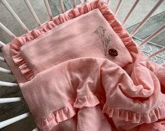 May include: A pink baby crib bedding set with ruffled edges. The bedding is made of a soft, breathable fabric.