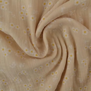 May include: Close-up of a beige fabric with a daisy pattern. The fabric is soft and flowing, with small white daisies and yellow centers scattered across the surface. The fabric is gathered in soft folds.