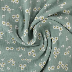 May include: A close-up of a soft, sage green fabric with a delicate floral pattern. The fabric is covered in small white flowers with yellow centers, creating a charming and airy design. The fabric is draped, showing its texture.