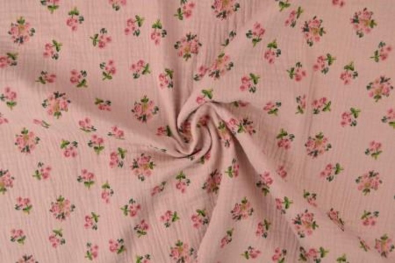 May include: Pink fabric with a floral pattern. The fabric has a crinkled texture and is covered in small clusters of pink flowers with green leaves. The fabric is gathered in a swirl in the center of the image.
