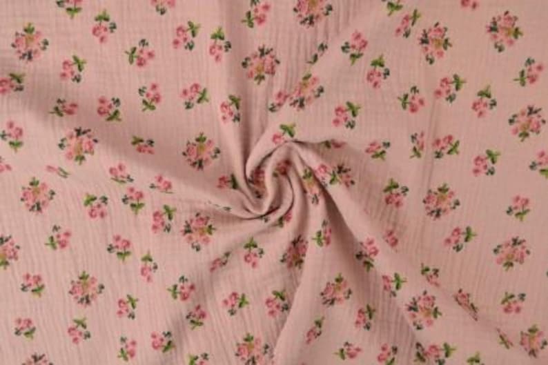 May include: Pink fabric with a floral pattern. The fabric has a crinkled texture and is covered in small clusters of pink flowers with green leaves. The fabric is gathered in a swirl in the center of the image.