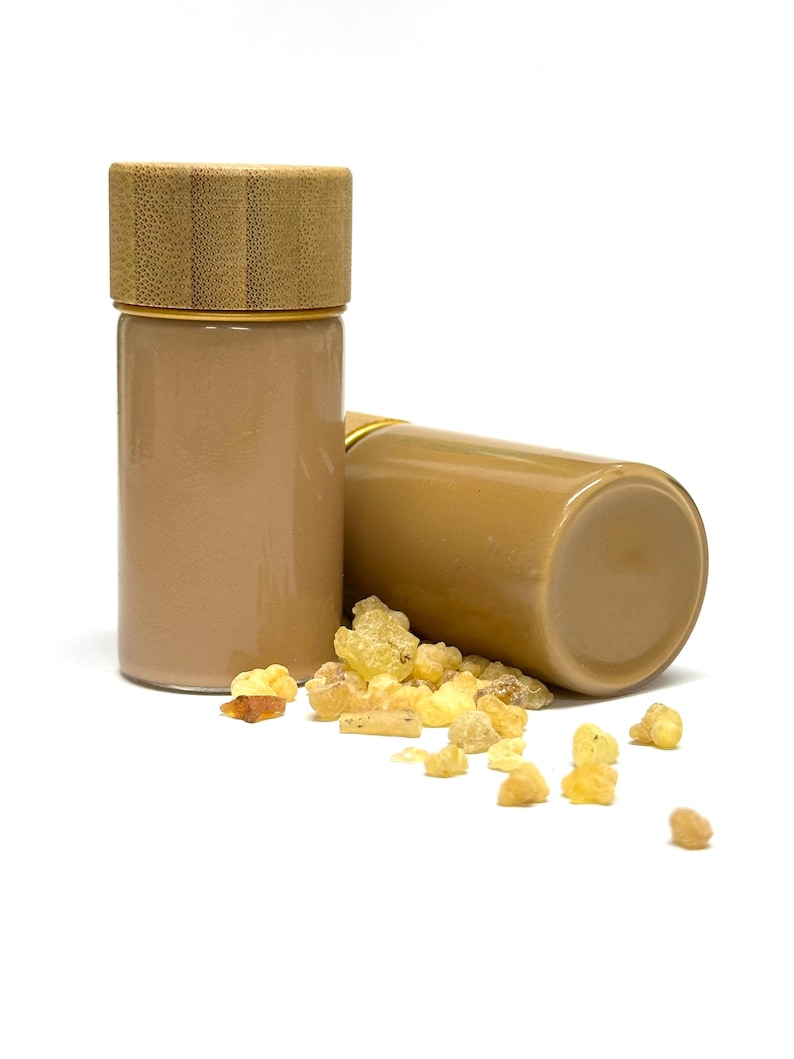 May include: Two small, cylindrical glass jars with light brown contents and bamboo lids. One jar stands upright, the other lies on its side. Scattered around are pieces of yellow-brown resin.