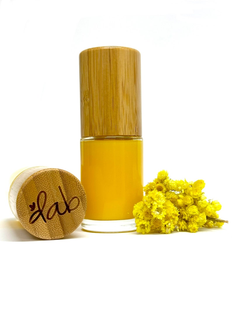 Pu&ograve; includere: Un siero giallo in una bottiglia di vetro con tappo e tappo in bamb&ugrave;. La bottiglia &egrave; etichettata con la parola "lab" in corsivo. Un rametto di fiori gialli &egrave; accanto alla bottiglia.