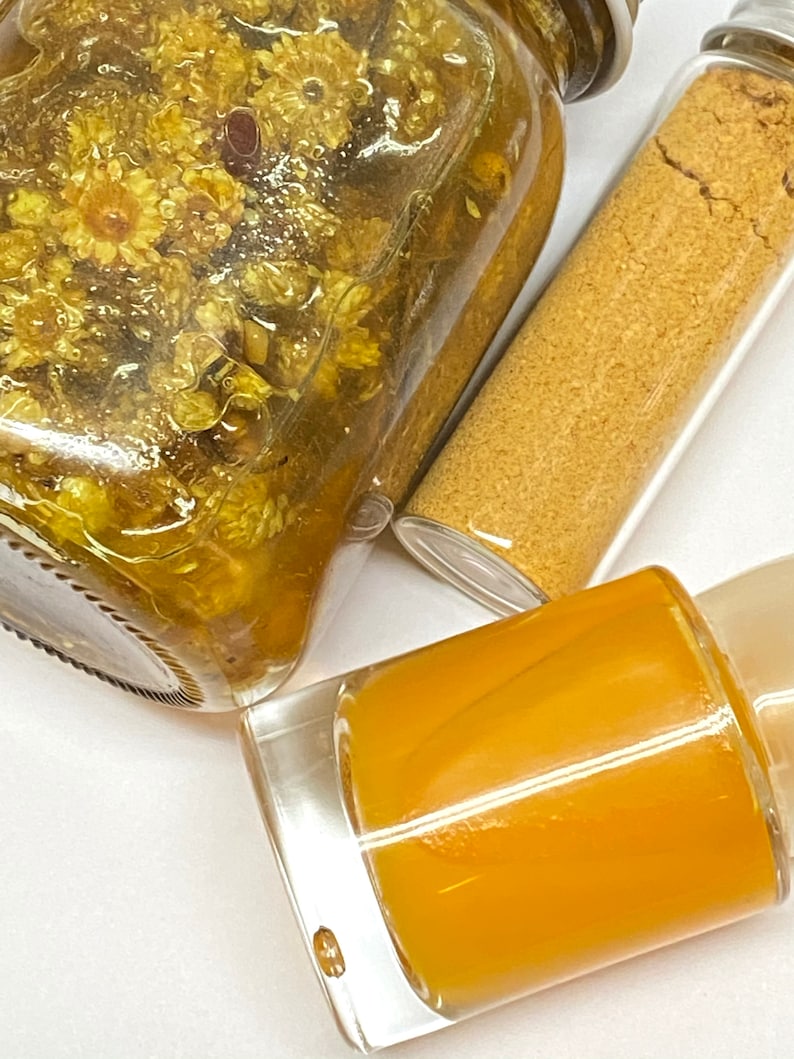 Pu&ograve; includere: Tre bottiglie di vetro contenenti liquidi gialli e fiori secchi. Le bottiglie sono su una superficie bianca.