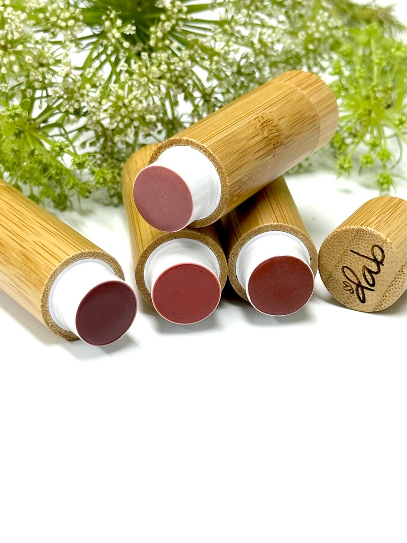 May include: Four bamboo tubes with white caps and different shades of pink and red lip balm inside. The tubes are stacked on top of each other. The top tube has the word "love" engraved on the side.