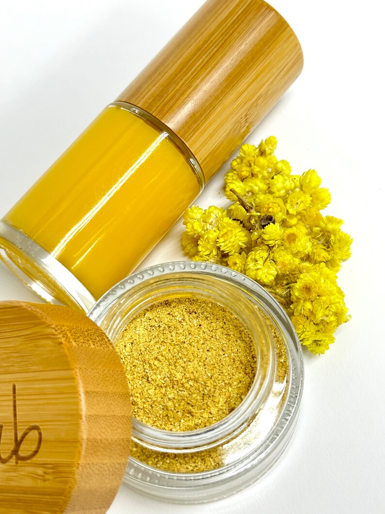Pu&ograve; includere: Un barattolo di vetro con un coperchio dorato e una polvere gialla all'interno. Il barattolo &egrave; appoggiato su una superficie bianca accanto a un piccolo mazzo di fiori gialli e una bottiglia di vetro con un liquido giallo e un tappo di legno.