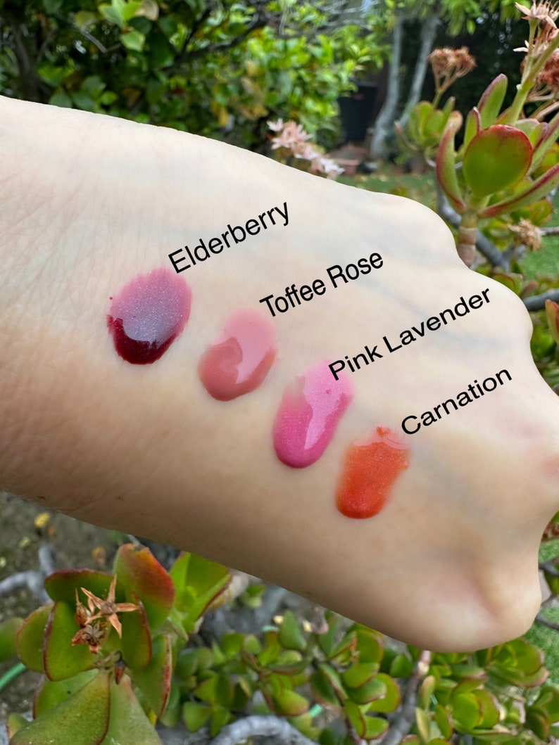 May include: Four distinct cosmetic product swatches labeled Elderberry, Toffee Rose, Pink Lavender, and Carnation. The Elderberry swatch is a deep purple, Toffee Rose is a muted mauve, Pink Lavender is a bright magenta, and Carnation is a vibrant orange.