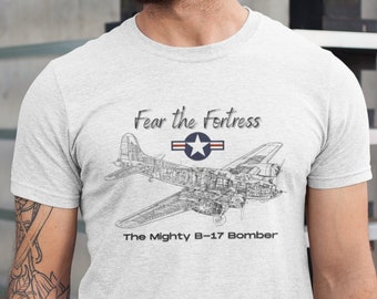 May include: A white t-shirt with a black and white illustration of a B-17 bomber plane. The text "Fear the Fortress" and "The Mighty B-17 Bomber" is printed on the shirt.