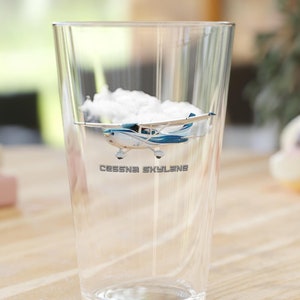 May include: A clear glass with water and a small airplane inside. The airplane is a Cessna Skylane and is flying through a small cloud. The text "Cessna Skylane" is printed on the bottom of the glass.