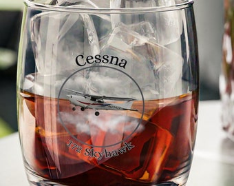 May include: A clear glass tumbler with a design of a Cessna 172 Skyhawk airplane. The glass is filled with brown liquid and ice cubes.