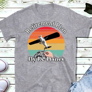 May include: A gray t-shirt with a vintage-style graphic of a plane and the text "Retirement Plan Fly RC Planes".