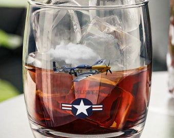 May include: A glass of whiskey with ice cubes and a vintage airplane graphic on the bottom of the glass. The graphic includes the text "MUSTANG" and a star.