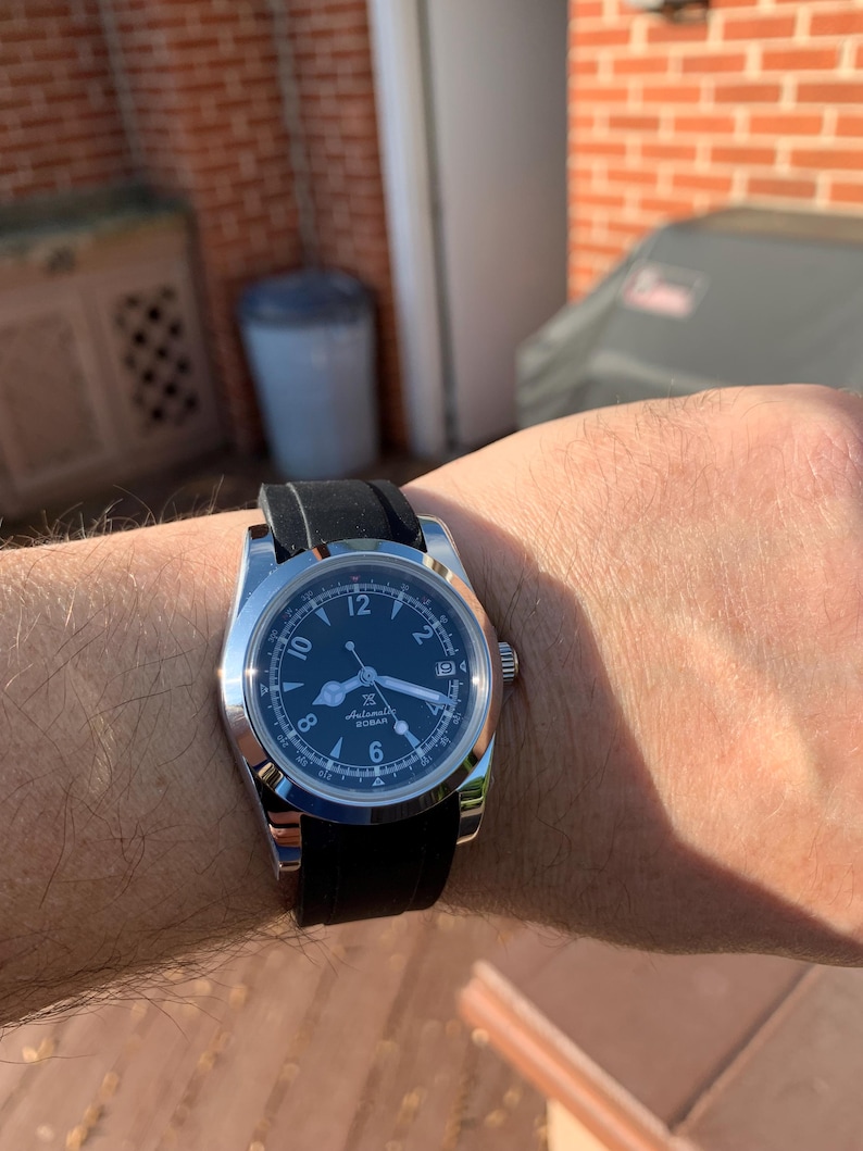 May include: A stainless steel wristwatch with a black dial and a black rubber strap. The watch face features white numerals and hands, with a date display at the 3 o'clock position. The watch is on a wrist.