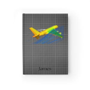 May include: A notebook with a gray grid pattern and a colorful illustration of an airplane. The airplane is yellow, green, and blue, with a design that appears to show airflow. The name "James" is printed in a simple font at the bottom.