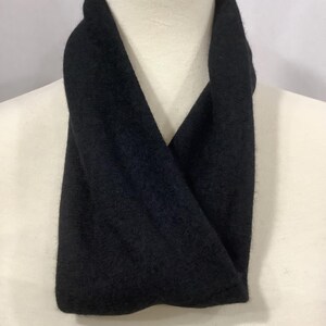 May include: A black infinity scarf displayed on a mannequin. The scarf is made of a soft, dark fabric and is draped around the mannequin's neck. The scarf's design is simple and classic, suitable for various outfits.
