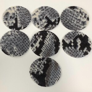 May include: Seven circular fabric patches featuring a monochromatic snakeskin pattern in shades of black, gray, and white. Each patch displays a textured, repeating scale-like design with irregular dark markings across the surface of the material.