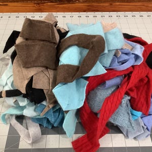 May include: A large, jumbled pile of assorted fabric scraps in various colors including brown, light blue, red, black, and grey. The collection consists of multiple textures and shapes of textile remnants layered together in a disorganized heap.