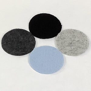 May include: Four circular fabric patches in shades of black, gray, and light blue are arranged against a white background. The patches have varying textures, with some appearing felt-like and others more woven.