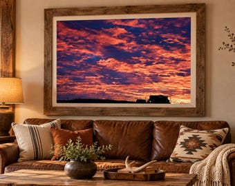 Könnte beinhalten: Ein großes, rechteckiges gerahmtes Wandbild, das einen leuchtenden Sonnenuntergang mit tief orangefarbenen, roten und violetten Wolken vor einem dunklen Himmel zeigt. Das Bild ist in einem dicken, verwitterten Holzrahmen.
