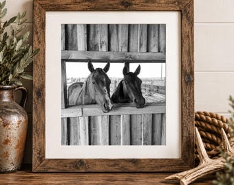 Könnte beinhalten: Ein schwarz-weiß Foto in einem quadratischen Holzrahmen zeigt zwei Pferde, die aus einer hölzernen Stallbox schauen. Die Pferde stehen nebeneinander und blicken durch die horizontale Öffnung der Stallwand nach draußen.