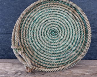 Könnte beinhalten: Eine kreisförmige Matte aus einem dicken, gewickelten Seil mit abwechselnden Strängen aus naturbeigen und tiefdunkelgrünen Fasern. Das Seil ist in einem durchgehenden Spiralmuster fest gewickelt und am Rand mit einer Schlaufe verknotet.