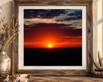 Könnte beinhalten: Ein quadratisches Wandbild in einem Rahmen, das einen leuchtenden Sonnenuntergang mit einer hellen orangefarbenen Sonne am Horizont, dunklen Wolken darüber und einer dunklen Landschaft darunter zeigt. Der Druck ist in einem verwitterten Holzrahmen.