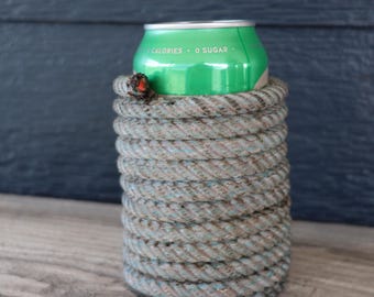 Könnte beinhalten: Eine grüne Aluminium-Getränkedose mit dem in Weiß aufgedruckten Text 0 CALORIES 0 SUGAR, umhüllt von einer dicken, gewickelten grauen Seilhülle. Das Seil ist fest um den Zylinder gewickelt und weist ein kleines, dunkles Knotendetail am oberen Rand auf.