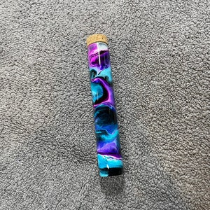 May include: A glass tube with a cork stopper filled with swirling blue, purple, and black paint.